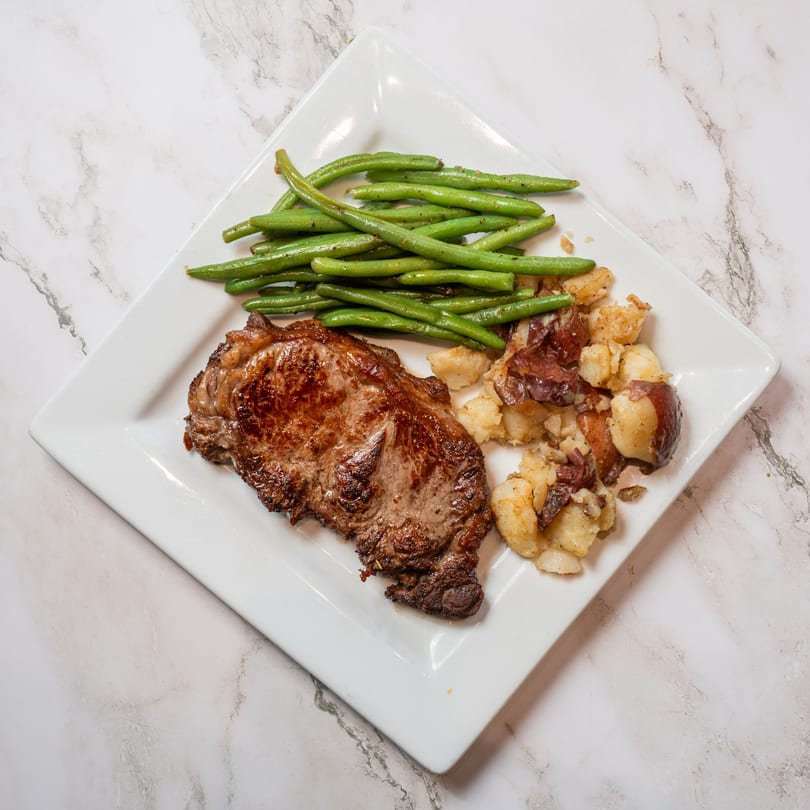 Grilled steak, green beans, and roasted potatoes on a white rectangular plate.