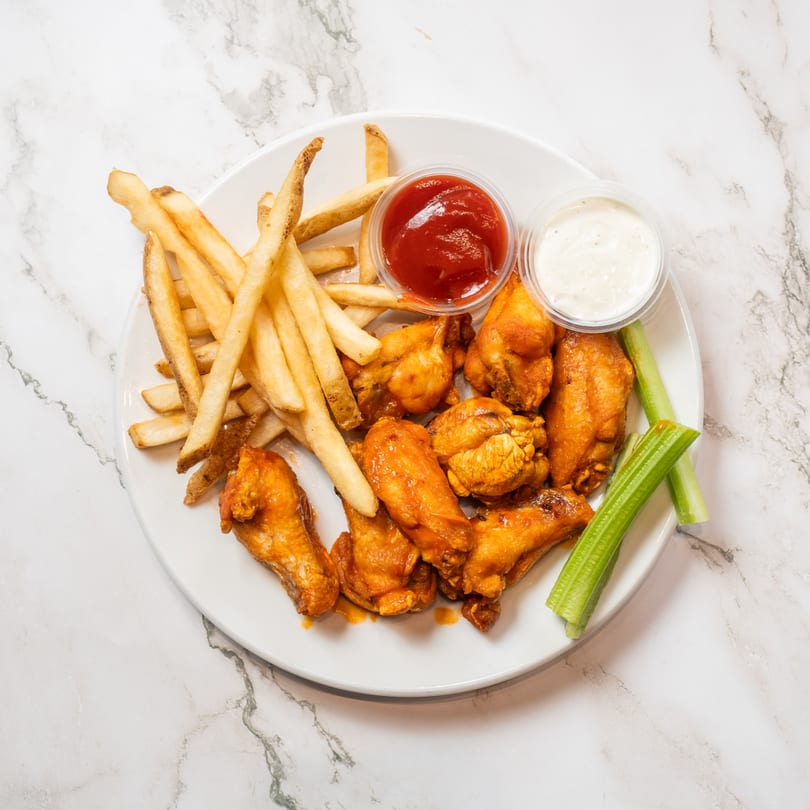 A plate of buffalo wings, french fries, celery sticks, ketchup, and ranch dressing.