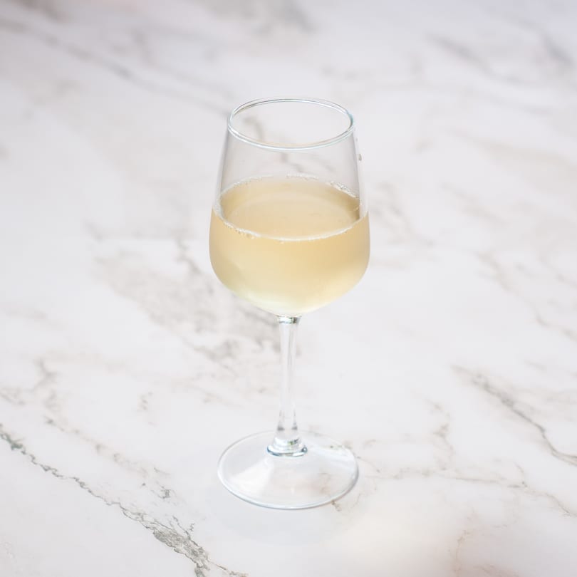 A champagne flute filled with a light yellow sparkling beverage, on a white marble surface.